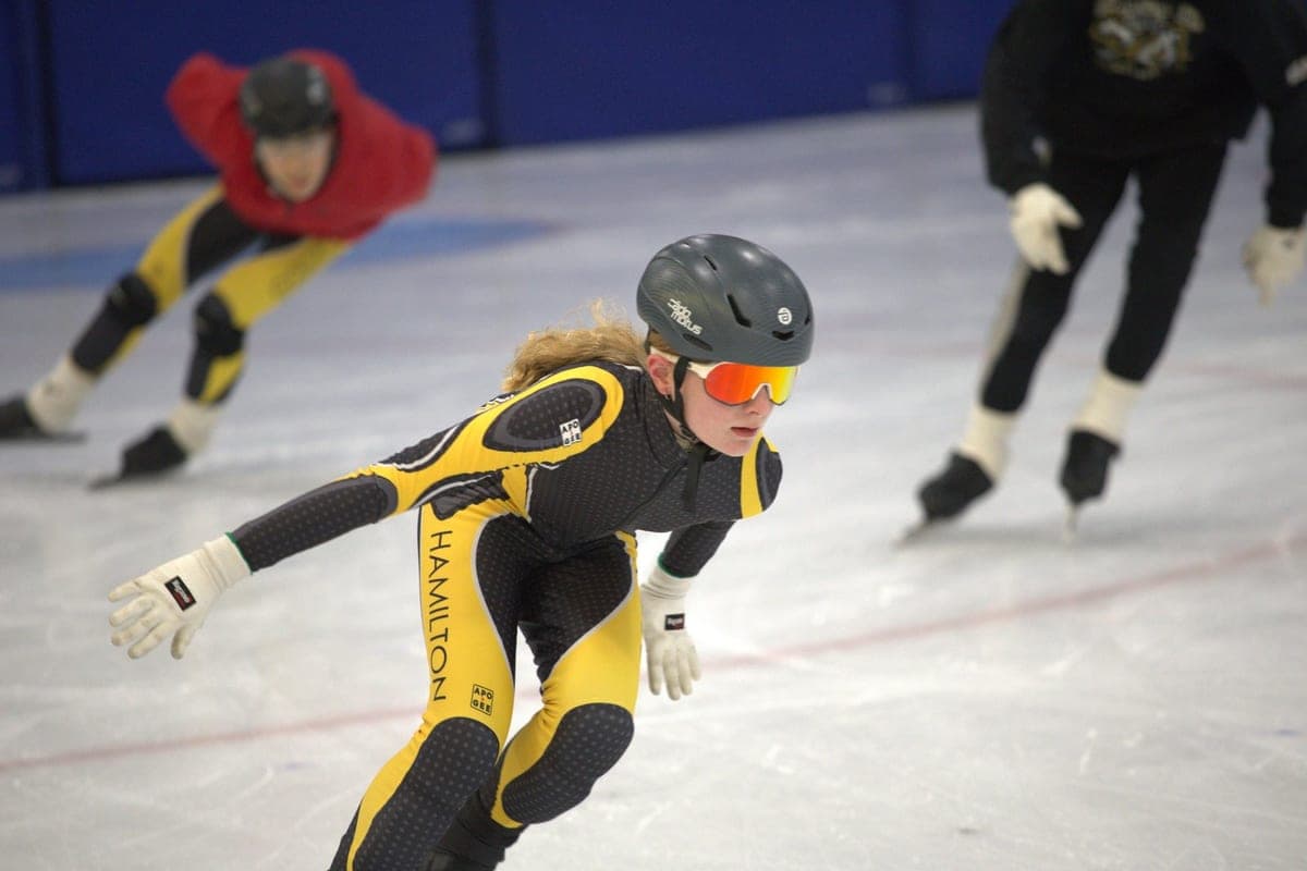 A Hamilton speed skater in club kit and orange goggles, mid-stride at practice.