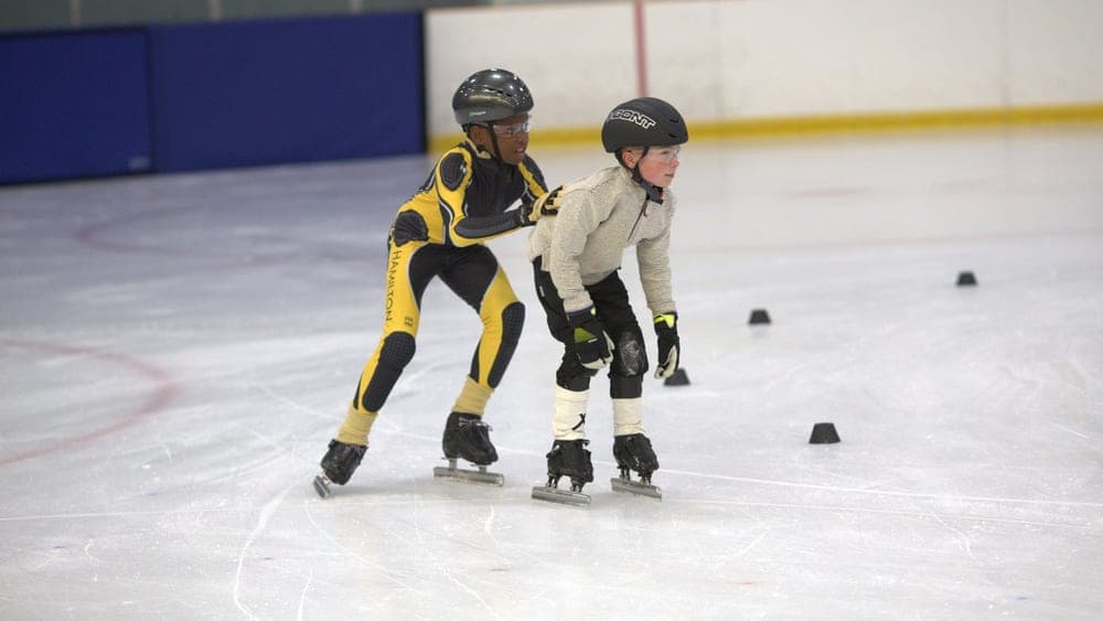 Two Learn to Speed Skate kids skating side by side during practice.