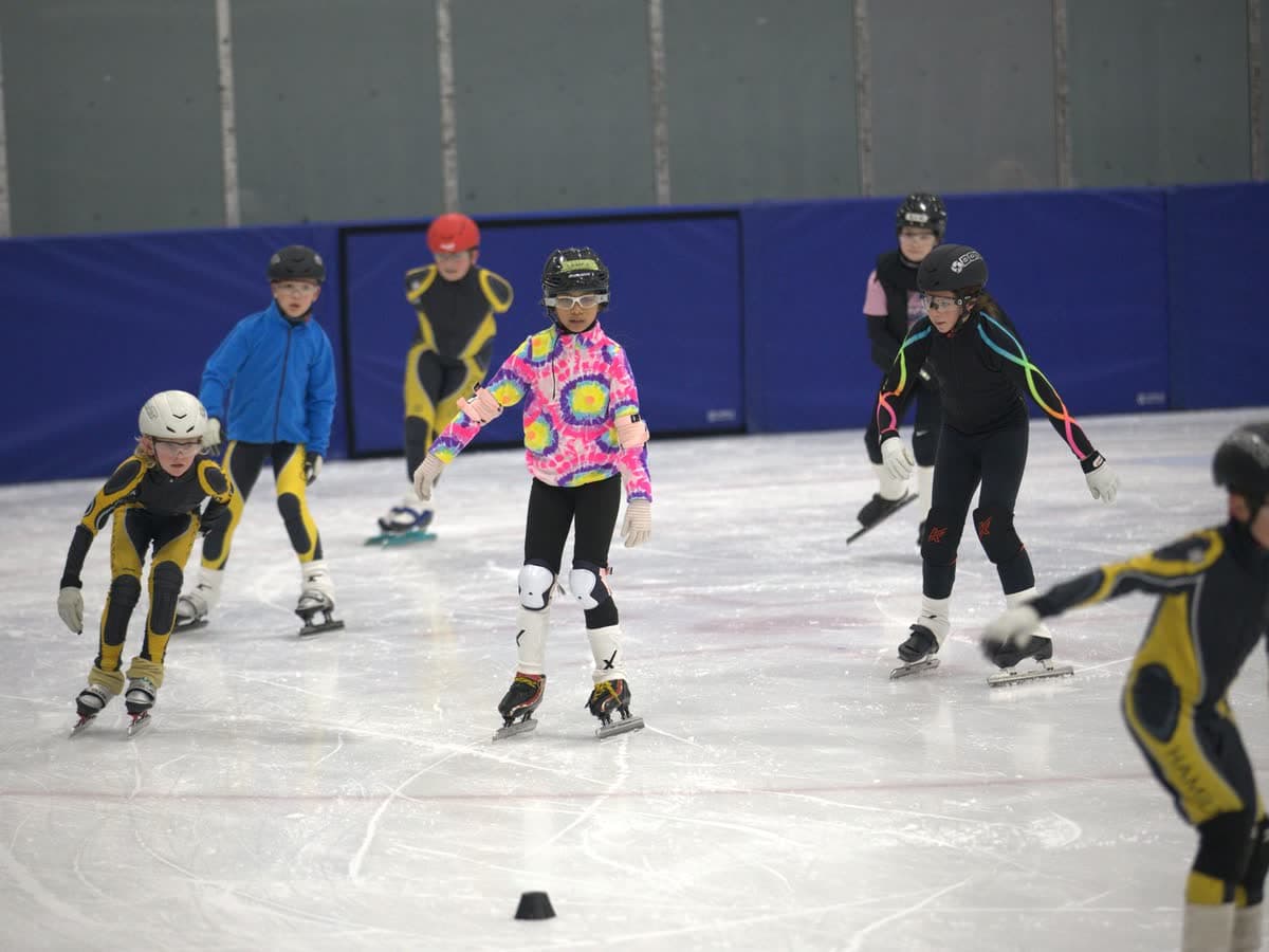 A spread of Learn to Speed Skate kids skating across the ice during practice, with pylons set out.